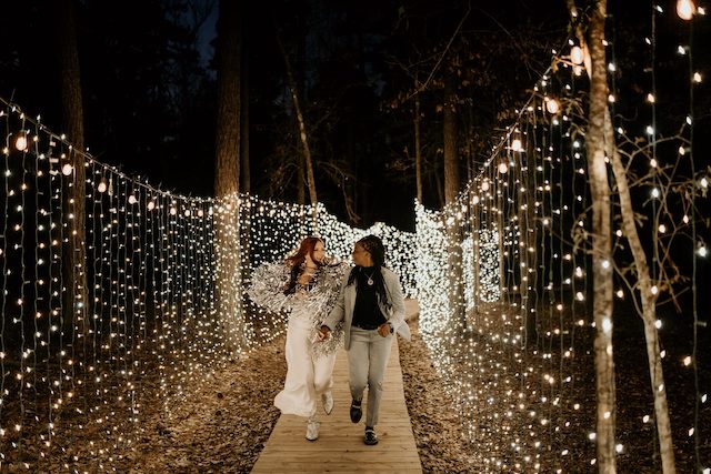 Two brides walking down a walkway covered in lights at wedding venues in Texas.