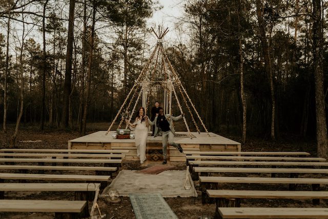 A bride and groom exchanging vows in front of a teepee in the woods at a unique Texas wedding venue.