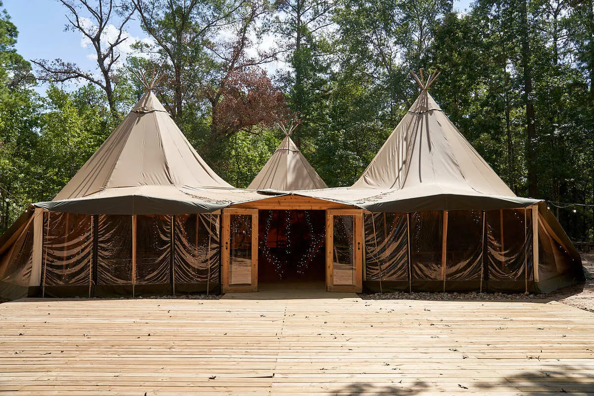 Outdoor wedding ceremony at The Shire Tipis in Huntsville, TX with Nordic tipis, pine trees, and a raised wood floor aisle