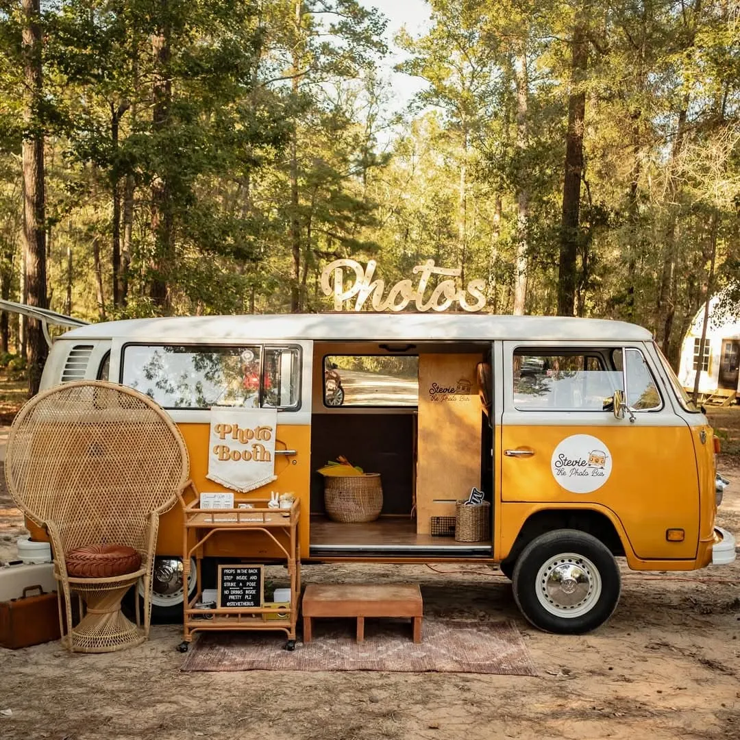 Vintage photo booth van in a forest setting, adorned with "Photos" sign, wicker chair, and decorative elements, enhancing the lively atmosphere for wedding celebrations at The Shire Tipis.