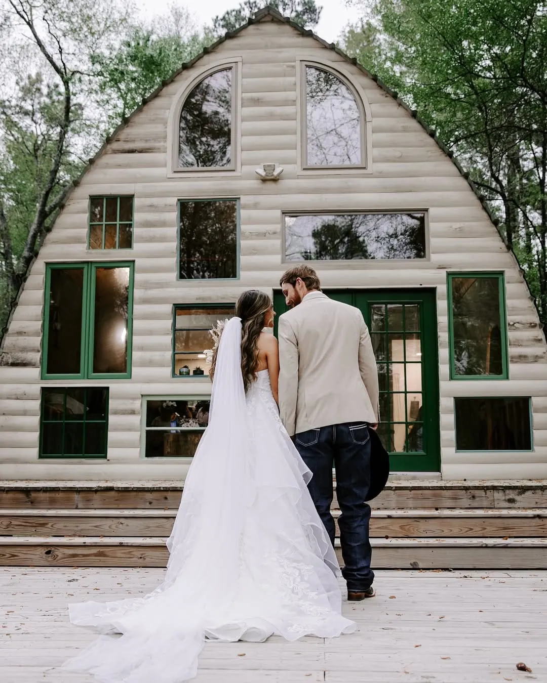 Bride and groom standing together in front of a rustic cabin with large windows, surrounded by greenery, showcasing an intimate wedding setting at The Shire Tipis.
